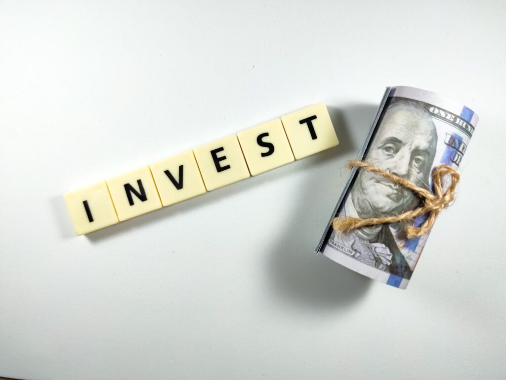 Dollar banknotes and scrabble letters with text INVEST on white background.Business concept